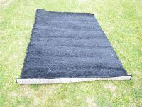 Full view of the black shag rug laid out on grass, showing size and black shag texture.