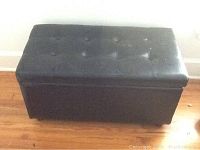 Black vinyl storage ottoman closed, showing rectangular shape with tufted button top and vinyl finish.