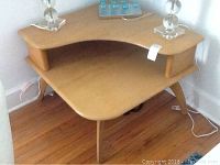 Full view of a light wood corner table with two-tier nook, positioned in a corner with crystal lamps on top.