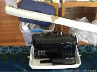 Photo showing black Singer sewing machine on white tray with carrying case and fabric box behind it.