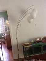 Full view of a tall metal floor lamp with three white spherical paper mache shades arcing out from the stand.