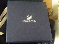 Blue Swarovski box with silver logo displayed closed.