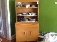 Full view of cabinet showing top glass shelf section, drawer and lower cabinet doors against green wall