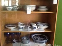 Full china set in wooden cabinet, includes cups, bowls, small and large plates, and stemware.
