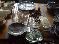 Photo of assorted items on table including Jack and the Beanstalk collector plates, clear glass dish, wood napkin holders, small glasses with colorful dots, pitchers and various ceramic bowls and plates.