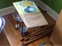 Metal and wood plant stand with two floral paintings and burlap cloth covering partly.
