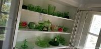 Photo of green glass cups, saucers, and various glassware pieces displayed on shelves in a cabinet.