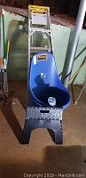 Photo shows a blue rolling bucket or tote in front of a black folding plastic step stool with textured surface, part of a metal 4 ft ladder visible in the background