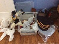 Photo showing a plastic bin with Native American dolls beside multiple stacked military hats including one Alpine style hat.