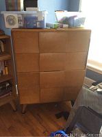 Front view of the chest of drawers with four curved drawer fronts, wooden surface with light wear, and tapered legs.