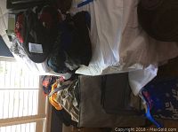 Wide view of assorted clothing including men's suit jacket, casual wear, and hats placed on chair and bed.