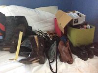 Overview of various men's and women's boots and shoes placed on a bed including boxes, bags, and different styles of footwear.