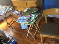 Photo showing Heywood Wakefield captain chair with upholstered seat and two wooden folding TV trays topped with folded fabric towels.