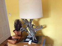 Full view of the driftwood lamp with two wooden bowls and faux plant on table against yellow wall