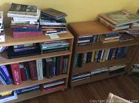 Photo showing two wooden bookcases side by side with multiple books on shelves and some items on top shelf.