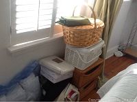 Wide view showing woven basket on top of a white plastic basket, stacks of linens below, and green curtain on the side.
