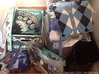 Photo of folded sweaters with blue and white patterns, and plastic bags with shoes and other items.