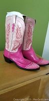 Pink and cream Lucchese cowboy boots on wooden surface showing side and front details