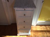 Front view of white cabinet showing four drawers, silver round knobs and some paint wear at base