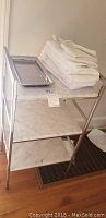 Metal framed shelf unit with three white marble shelves, towels and tray on top