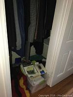 View inside hallway closet showing several hanging jackets and clothing along the rod; floor space has multiple stacked plastic bins and boxes with organizers