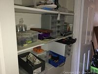 Full view of three shelves with plastic storage containers, staplers, and office supplies like pens and highlighters.