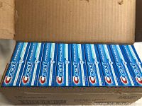 Opened cardboard box showing multiple blue and white rectangular toothpaste boxes lined up.