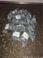 Multiple small clear plastic bags filled with metal wood screws scattered on floor, showing quantity and packaging.