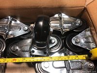 Box with 12 hard rubber casters including chrome metal mounting plates and wheels, measuring about 4 inches, comfortable close-up angle showing wheel and metal parts.
