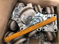 Box of 12 swivel wheel castors with nylon wheels and metal mounting plates, ruler shows 3 inch size