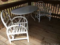 Oval fiberglass table and two white PVC patio chairs with vinyl webbing on a wood deck.