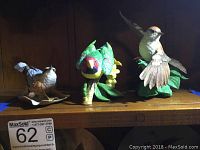 Three porcelain bird figurines from Lenox displayed on a wooden shelf: Red-breasted Nuthatch, Plum-headed Parakeet, and Chipping Sparrow.