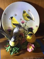 Two yellow Lenox porcelain bird figurines in front of Bradex plate with goldfinches on thistle background.
