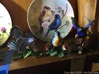 Three Lenox porcelain bird figurines displayed on a wooden surface with a ceramic bird plate behind them