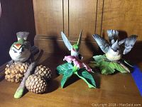 Overall view of three Lenox bird figurines on wooden surface under warm light, showing detailed painting and natural bases.