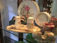 Glass shelf display with Lenox porcelain items including plates, shakers, napkin rings, candy dish, and trinket box.