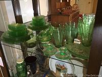 Photo of entire collection of 24 pieces of green Depression glass including plates, berry dishes, glasses, candle holders, hand juicer, smooth bowl and serving bowl.