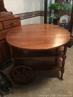Full view of the wooden tea cart with folded sides, showing large wooden wheels and lower shelves.