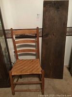 Vintage wooden ladder back chair with woven cane seat in front of wall and near wooden barn shelf plank.