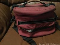 Red padded camera bag case closed, showing exterior zippered compartments and carrying strap.