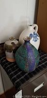 Three pottery jugs on a checker-pattern cloth including one with blue eagle symbol.