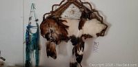 Full view showing two Native American themed wall hangings; the larger features a leather woven basket, feathers, and rabbit fur; the smaller comprises a decorated horseshoe with blue-green leather and beads.