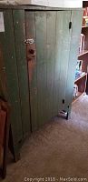 Front view of green antique rustic wood cabinet with a single door featuring a metal latch and knob, showing worn paint.