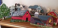 Photo showing a group of wooden decorative art pieces with a red barn with 'SEE 7 STATES FROM ROCK CITY' on the roof, farm silo, tobacco barn, and small houses arranged on a shelf.