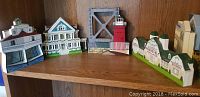 Four handcrafted wooden models including lighthouse, bridge, and houses displayed on a wood shelf