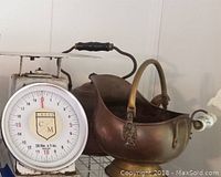 Photo of copper tea kettle and brass pot placed on display shelf alongside kitchen scale.
