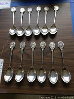 12 sterling silver spoons arranged neatly on a wooden surface, showing the flower motif on the handle ends. Each spoon is about 5 inches long.