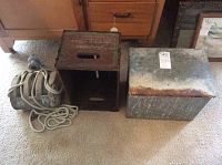 Old tin dairy cooler, wooden crate, and pulley block grouped together on carpeted floor.