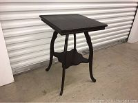 Side view of the ebony small table showing the four curved legs and decorative edges on table top.