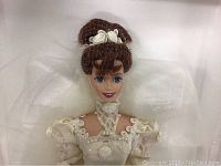 Close-up image of Barbie doll's head and upper body showing red hair styled with white rose accessory and lace pearl detailed wedding gown.